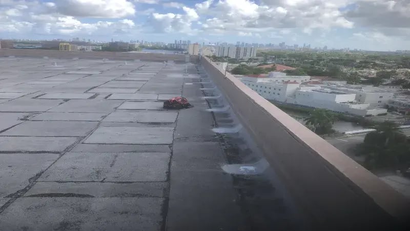 A view from a rooftop showing a red cleaning machine on a concrete surface with a city skyline in the background.