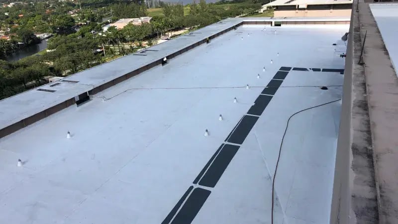 Aerial view of a flat commercial building roof with markings and ventilation in a suburban landscape.